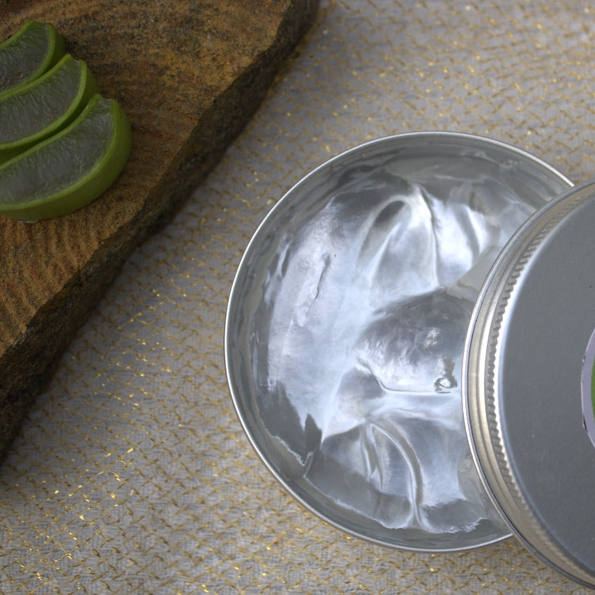 Metal tin with aloe vera gel on a stone surface with lime slices.