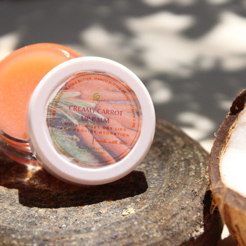 Jar of Creamy Carrot lip balm on a stone surface with a coconut half beside it.